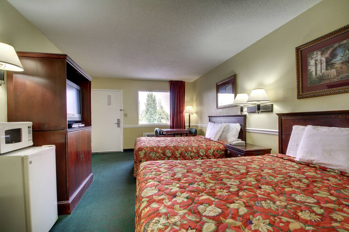 Quarto de hotel com duas camas, uma escrivaninha, micro-ondas e um pequeno frigorífico.
