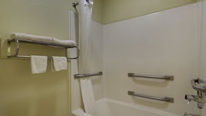 A bathroom with a bathtub, a shower curtain, and a towel rack with two towels. - Key West Inn - Montgomery (Montgomery)