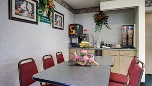 A dining area with a table, chairs, a coffee machine, and a sign indicating breakfast hours. - Key West Inn - Montgomery (Montgomery)