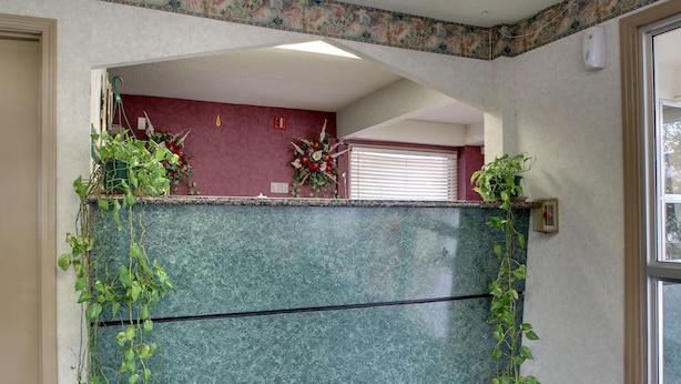 A reception area with a green marble counter, potted plants, and a red wall. - Key West Inn - Montgomery (Montgomery)