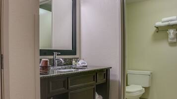 A bathroom with a sink, mirror, and toilet. There are towels on a rack and a tissue box on the counter.