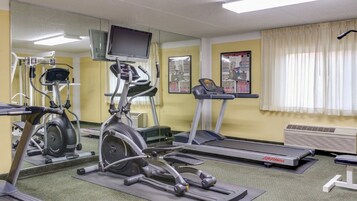 Une salle de sport équipée de machines de cardio, d’un tapis de course et d’un mur recouvert de miroirs.