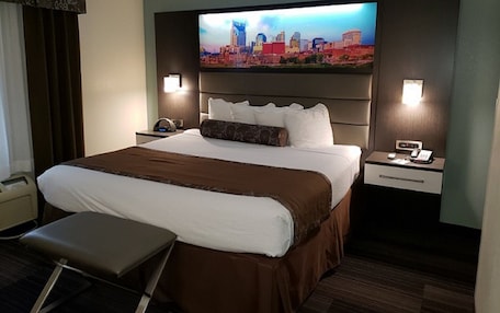 A hotel room with a large bed, a flat-screen TV mounted on the wall, a bedside table with a phone, and a small desk with a chair.