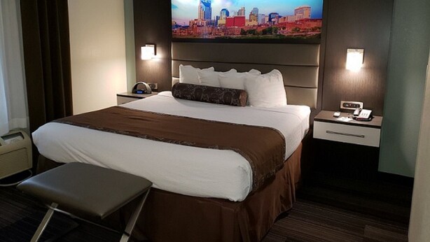 A hotel room with a large bed, a flat-screen TV mounted on the wall, a bedside table with a phone, and a small desk with a chair. - Club - Hotel Nashville Inn & Suites (Nashville)