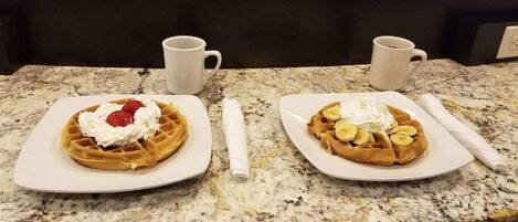 Two plates of waffles with toppings on a granite countertop.