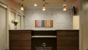 A reception desk with a Club-Hotel Nashville logo, a modern light-colored wall, and a decorative painting above it. - Club - Hotel Nashville Inn & Suites (Nashville)