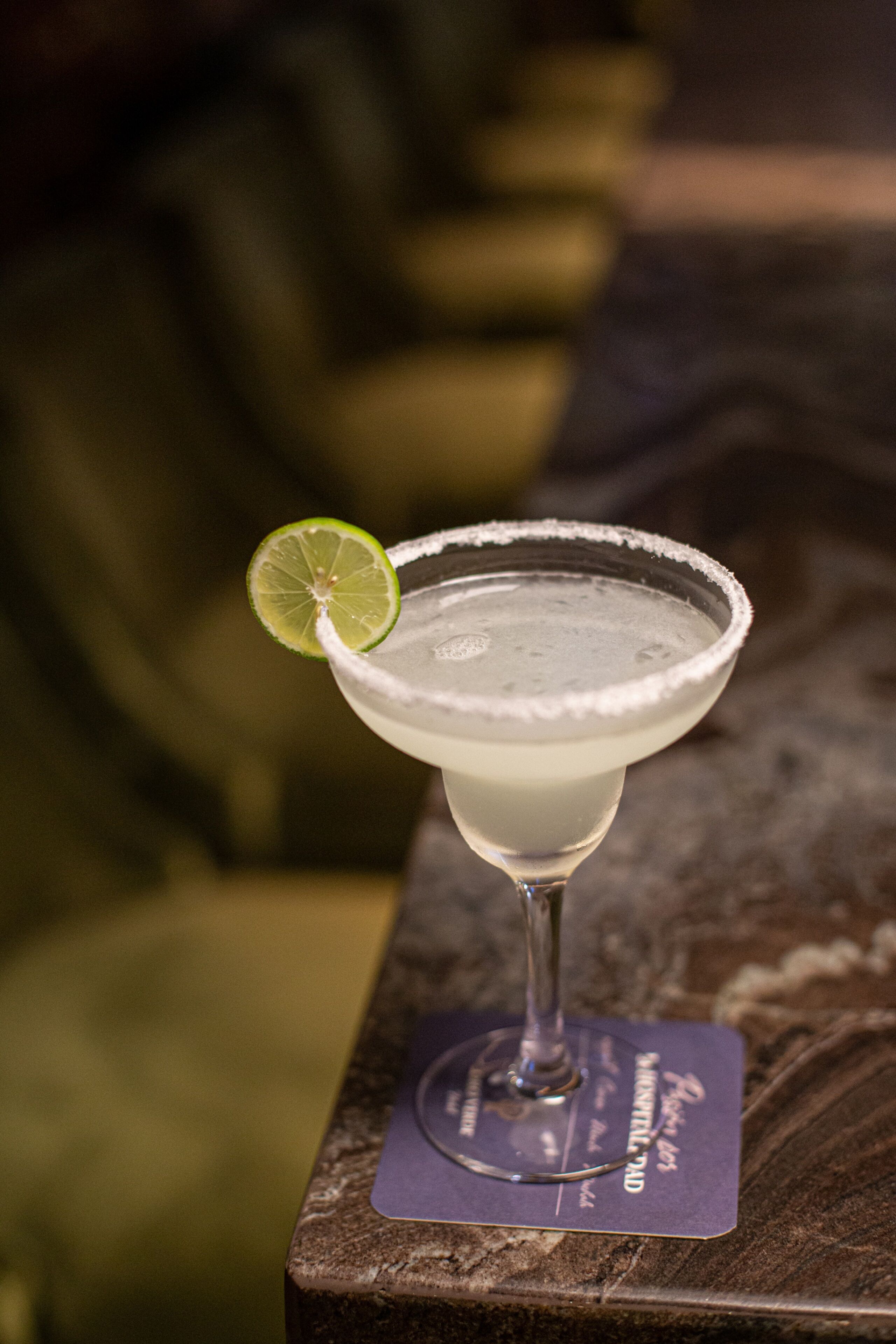 A margarita cocktail with a lime garnish on a bar counter.