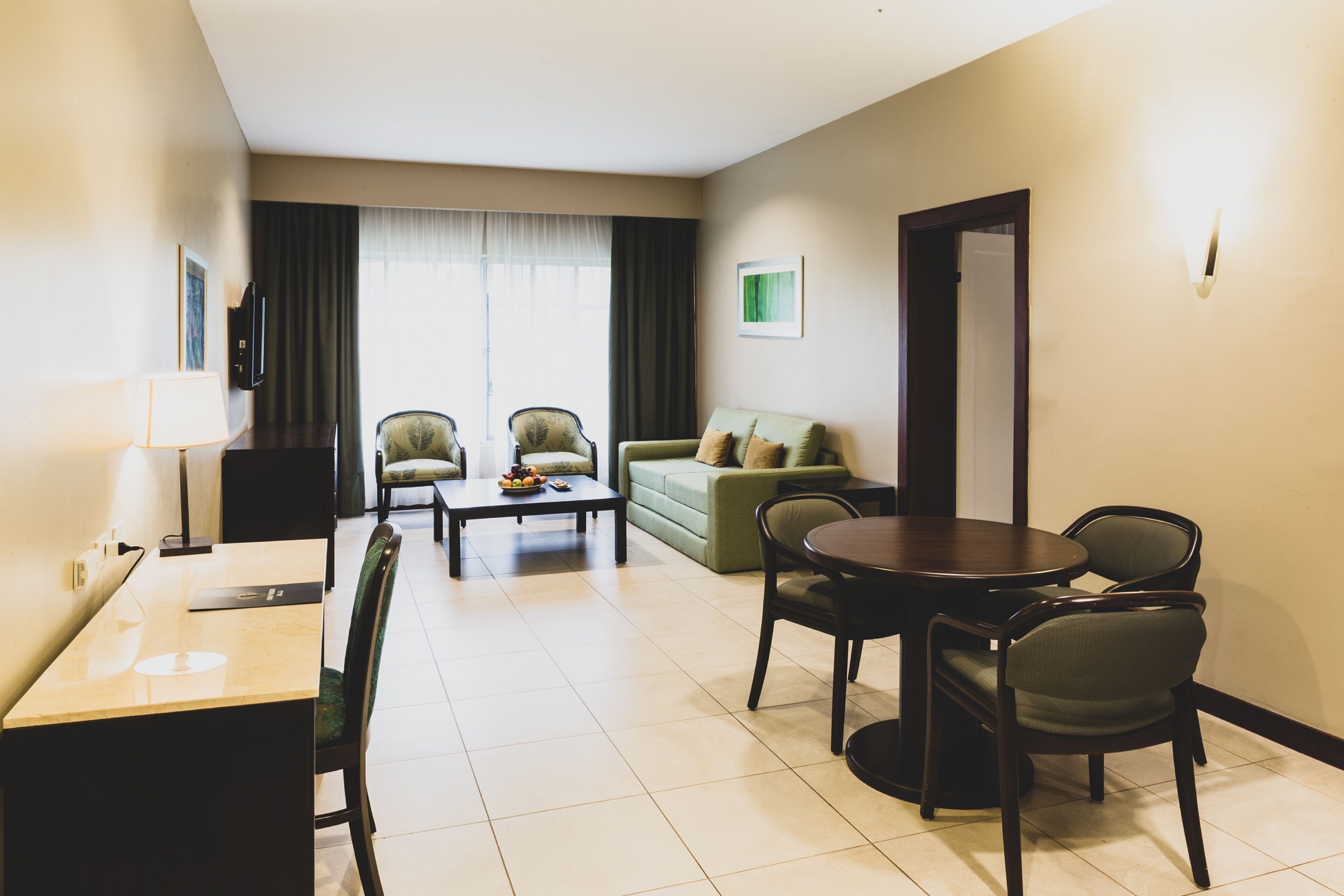 Habitación de hotel con comedor, sofá, televisor y puerta.