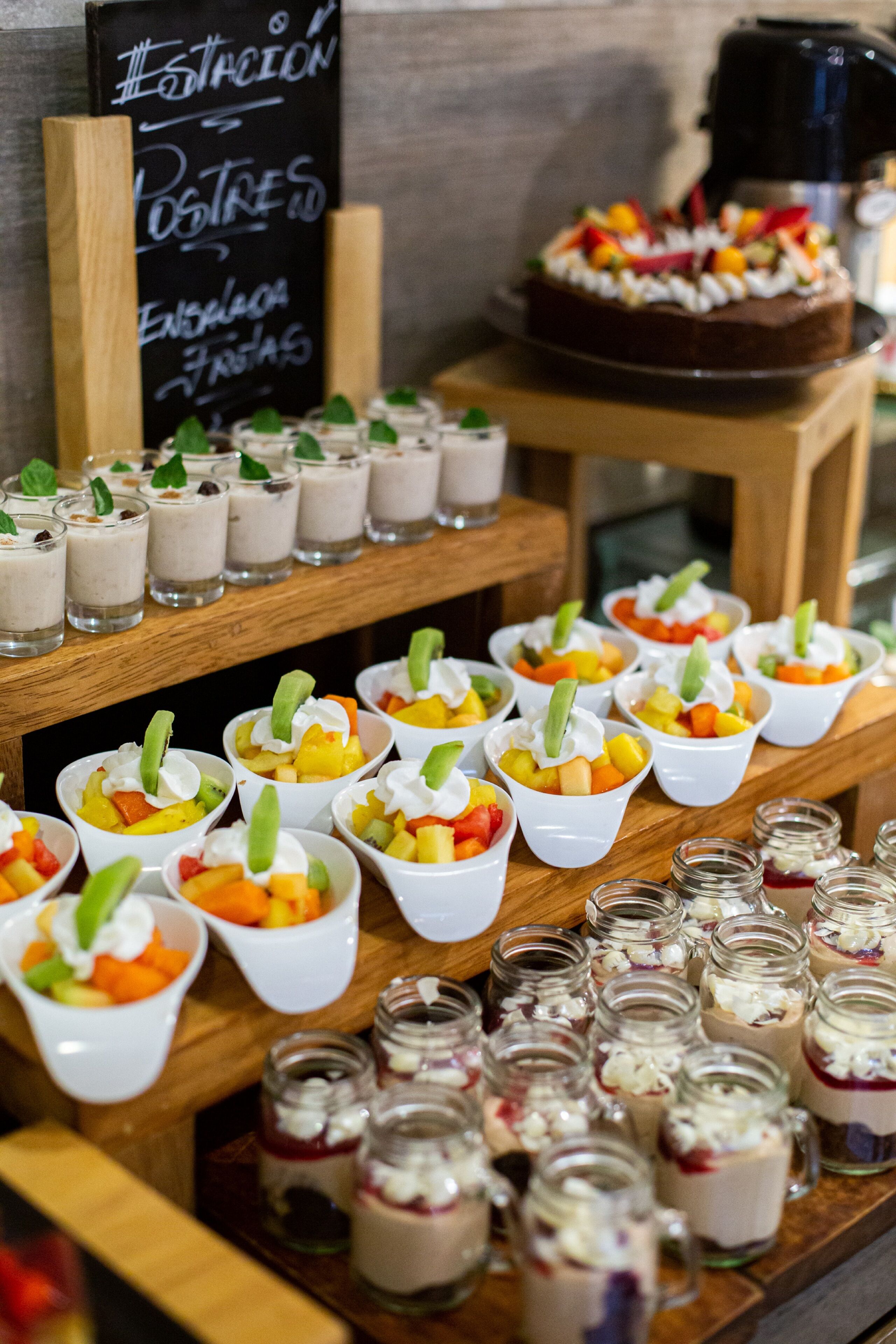 Una presentación de postres con diversas frutas y postres a base de crema en pequeños vasos y tarros.