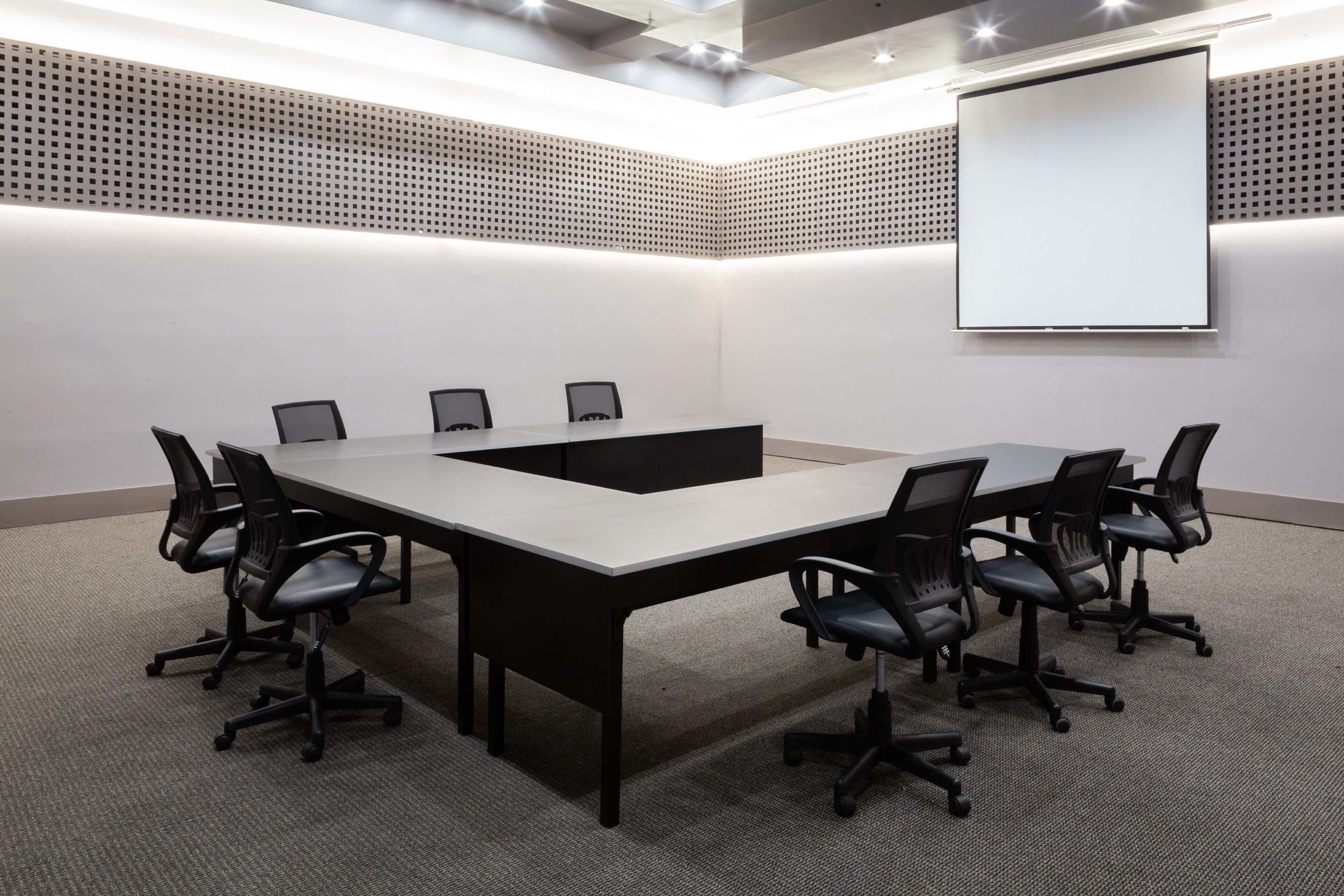 A conference room with a long table, six chairs, a projector screen, and a perforated ceiling.
