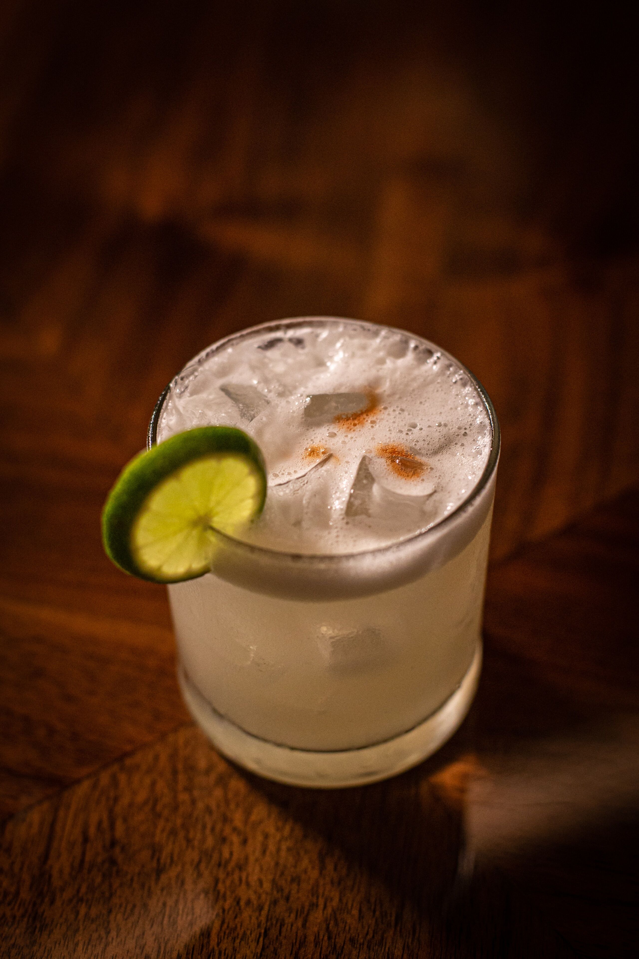 A glass of iced beverage with a lime wedge garnish on a wooden surface.