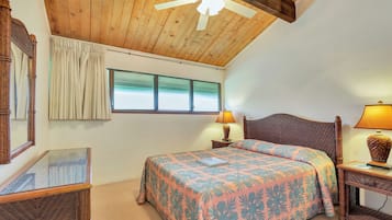 A bedroom with a wooden ceiling, a bed with a floral bedspread, a nightstand with a lamp, and a window with curtains.