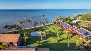 Vue aérienne d’un complexe hôtelier doté d’une piscine, de panneaux solaires, de palmiers et d’une plage.