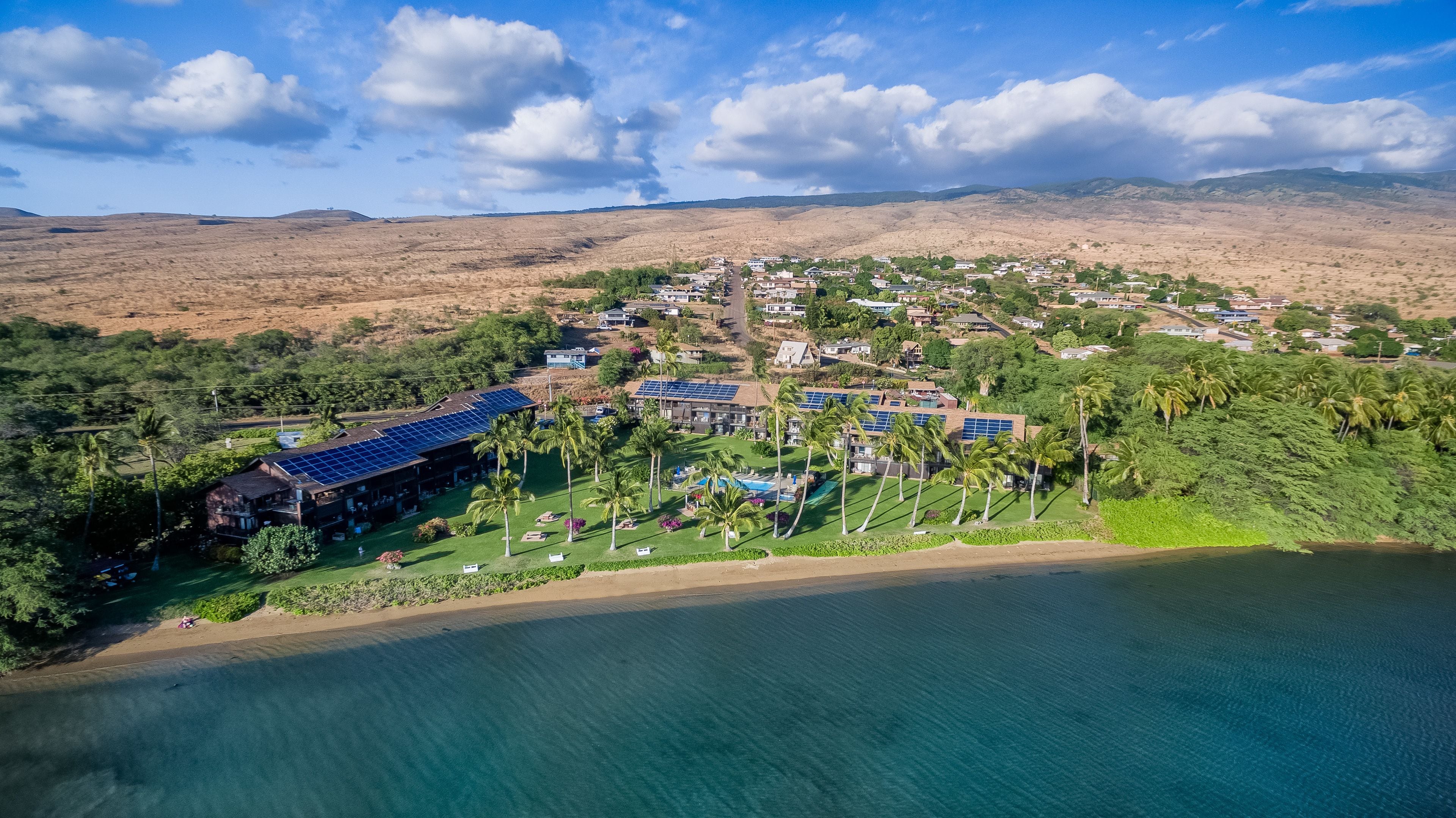 An aerial view of a coastal resort with multiple buildings, solar panels, and a beachfront.