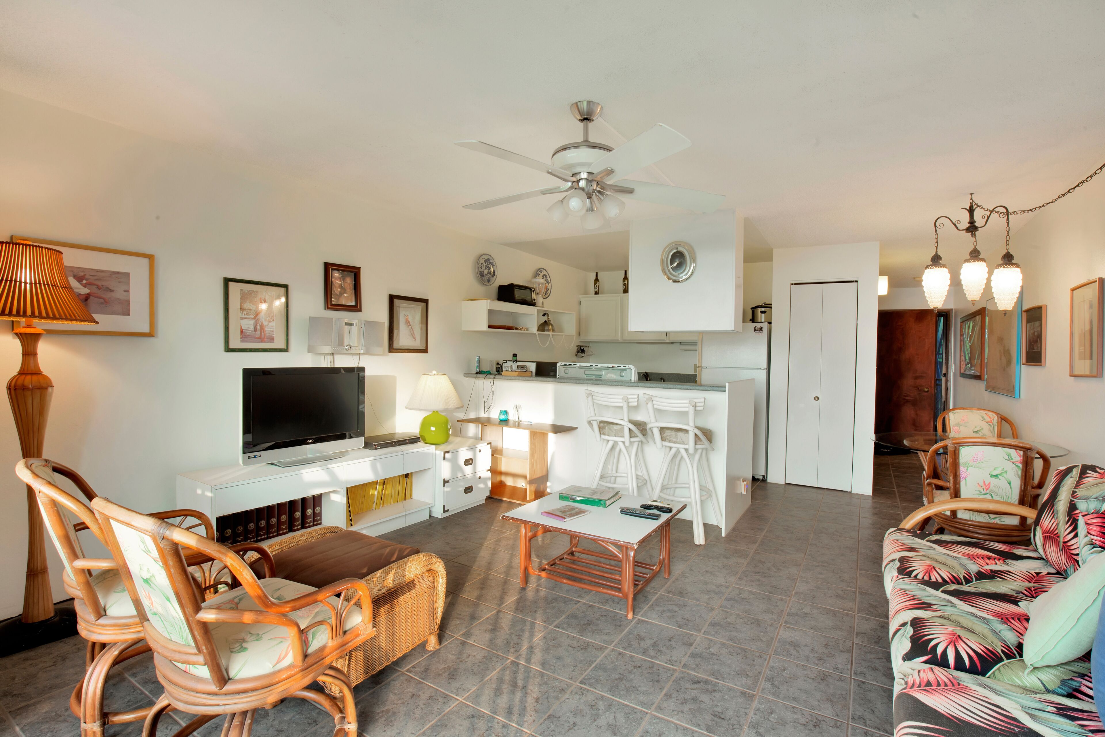 A living room with a television, wicker chairs, a sofa, a coffee table, and a ceiling fan.