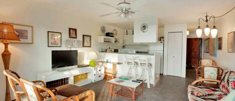 A living room with a television, wicker chairs, a sofa, a coffee table, and a ceiling fan.