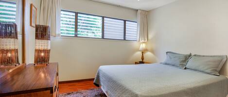Un dormitorio con cama, cómoda de madera y ventana con persianas.