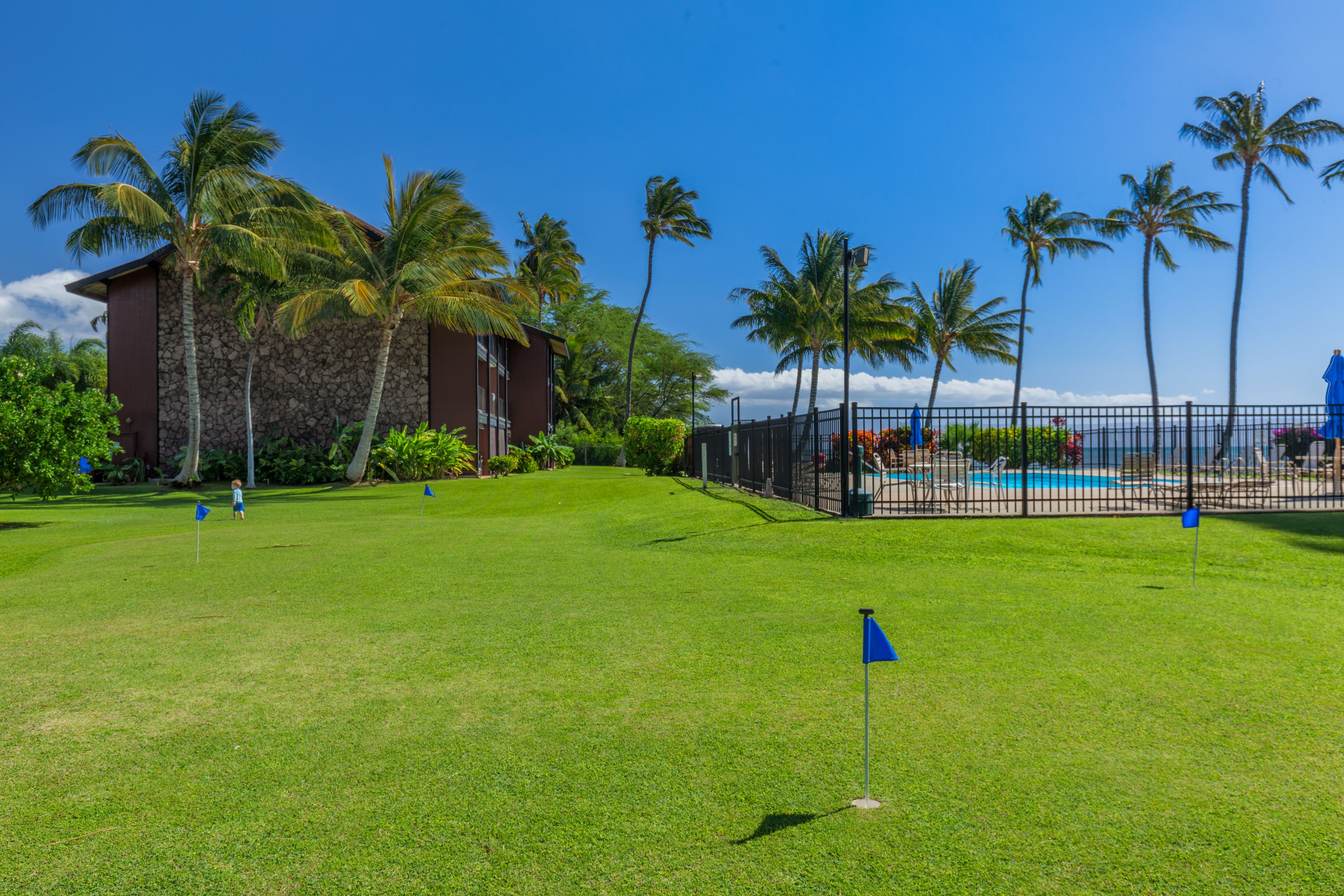Un terrain de golf bien entretenu, avec un ciel bleu dégagé, des palmiers et une piscine visible au loin.