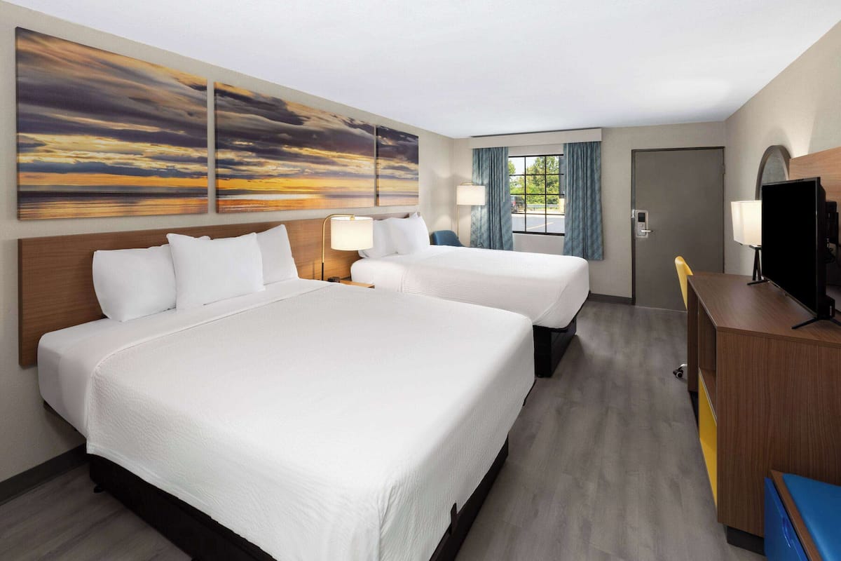 A hotel room with two beds, a desk, a TV, and artwork on the wall.