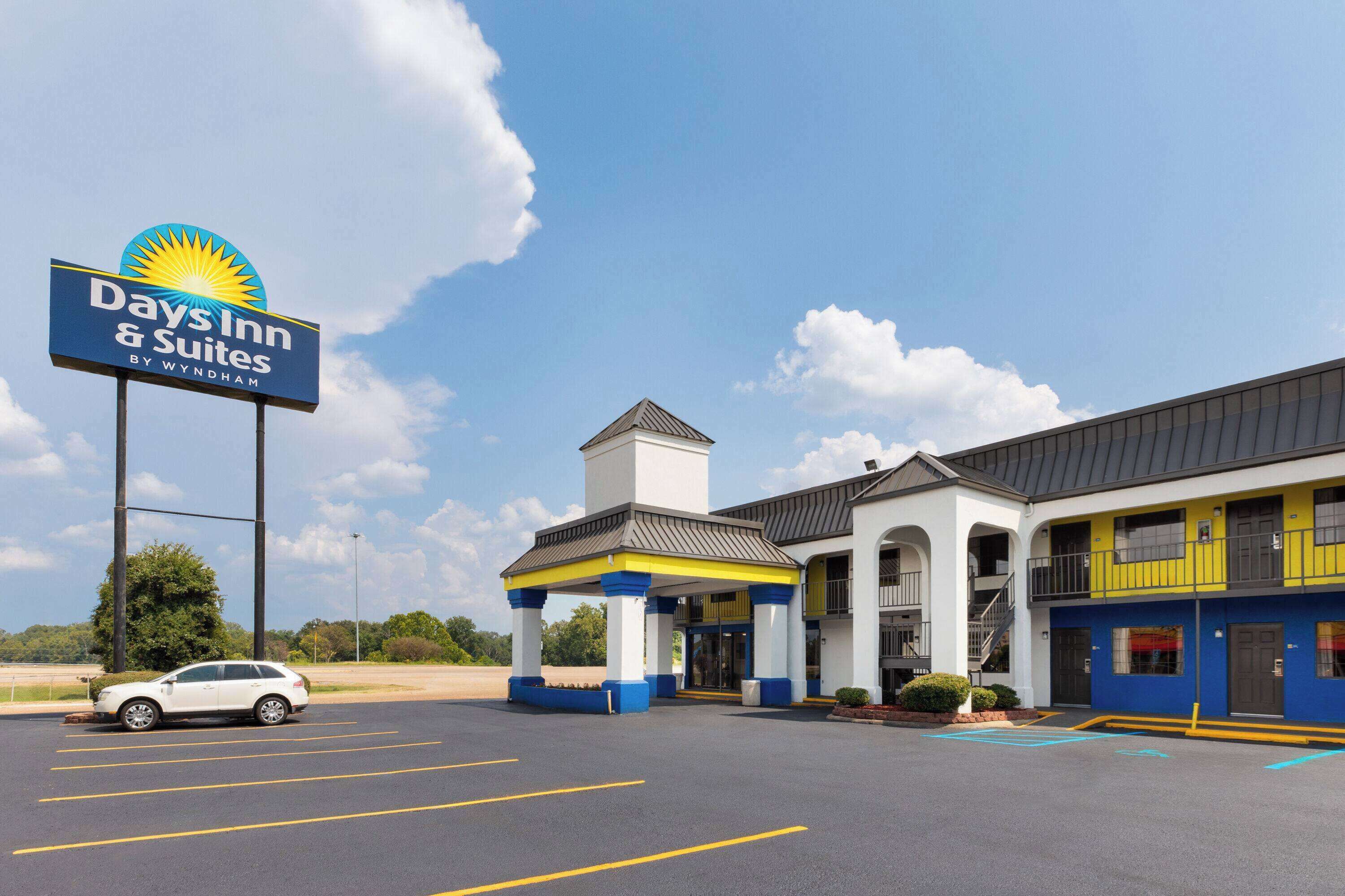 A Days Inn & Suites by Wyndham with a parking lot, a covered entrance, and a two-story building with blue and yellow exterior.
