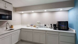 Una cocina moderna con armarios blancos, microondas, cafetera y refrigerador pequeño.