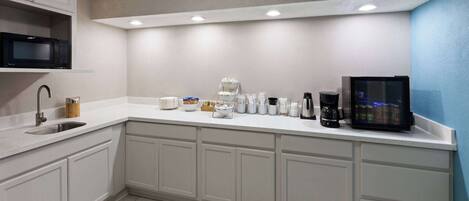 A modern kitchen with white cabinetry, a microwave, a coffee maker, and a small refrigerator.