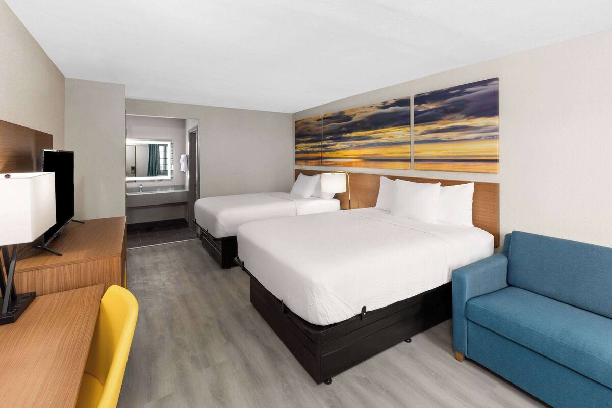 A hotel room with two beds, a desk with a chair, a TV, and a large painting on the wall.