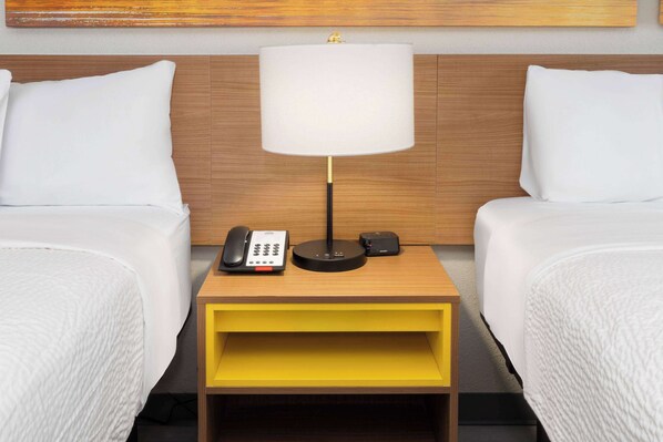 A hotel room with two beds, a bedside table with a lamp, a phone, and a small speaker.