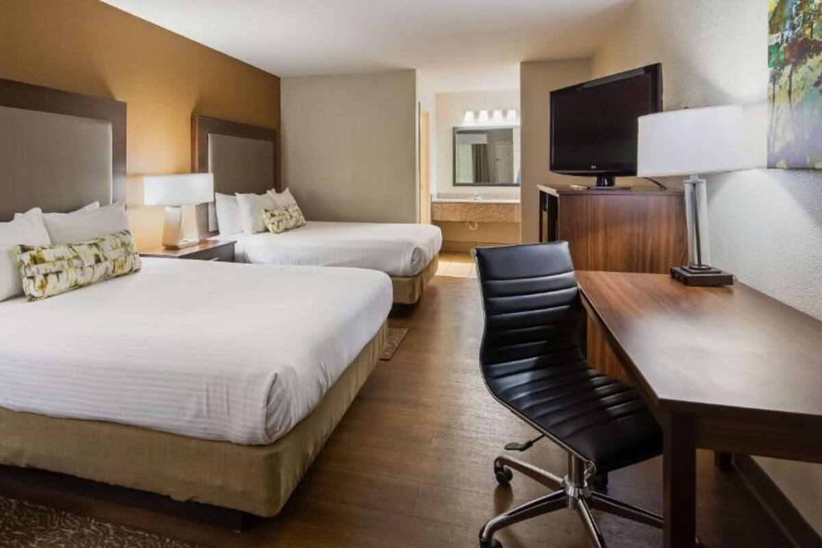 A hotel room with two beds, a desk, a chair, a television, and a bathroom mirror.