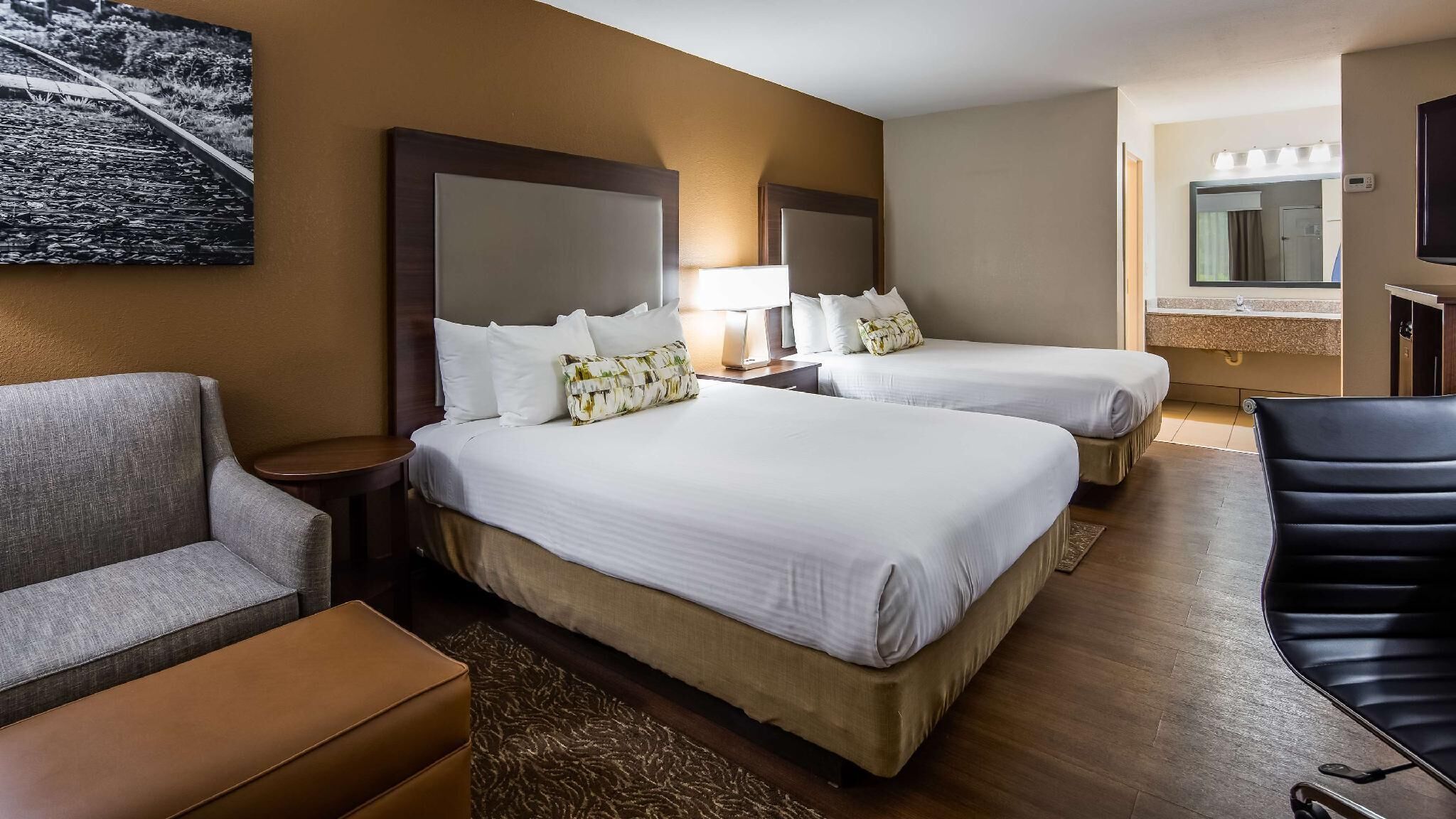 A hotel room with two beds, a sofa, a chair, a small table, and a painting on the wall.