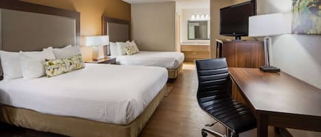 A hotel room with two beds, a desk, a chair, a TV, and a bathroom visible in the background.