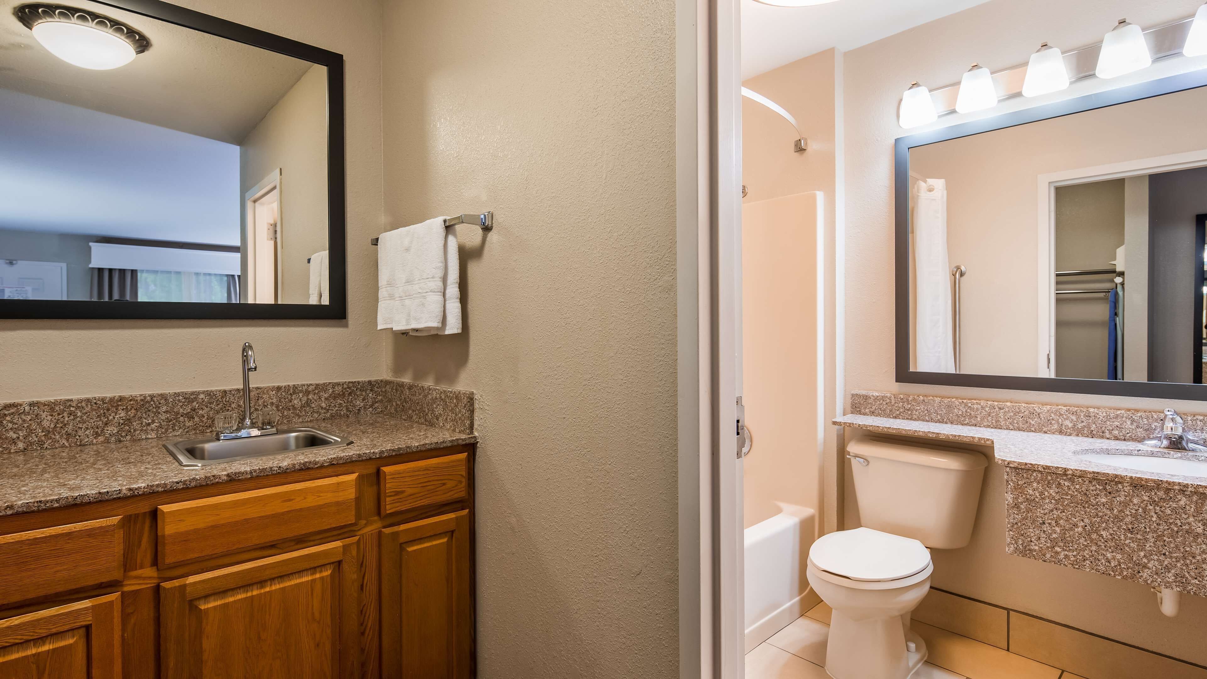 A bathroom with a granite countertop sink, wooden cabinets, a white toilet, and a large mirror.