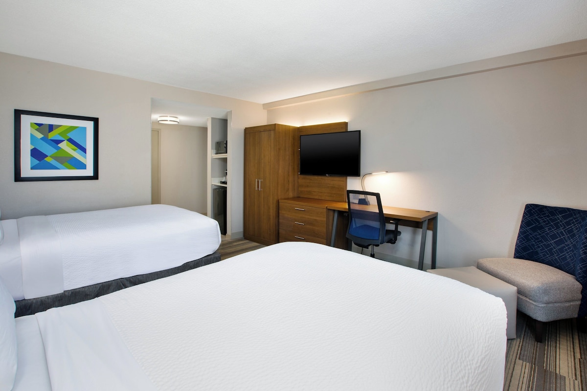 Habitación de hotel con dos camas, un escritorio con silla, televisión y un cuadro en la pared.
