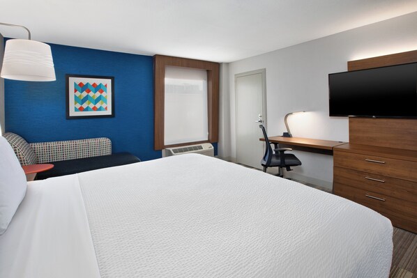 A hotel room with a large bed, a desk with a chair, a television, and a window with blinds.