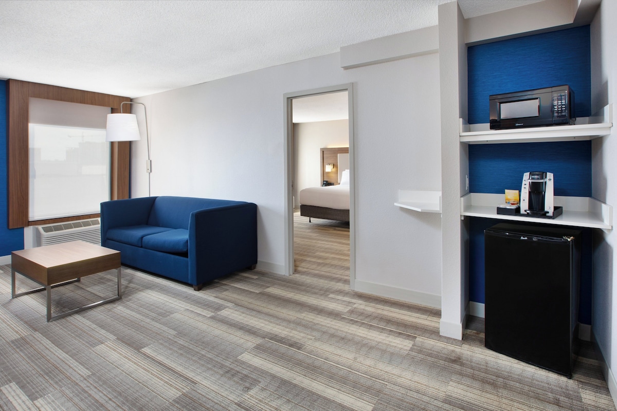 Habitación de hotel con un sofá azul, una mesita, un microondas y un refrigerador.