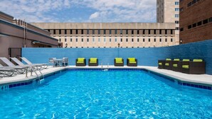 Une piscine avec des chaises longues et, en arrière-plan, un immeuble de grande hauteur.