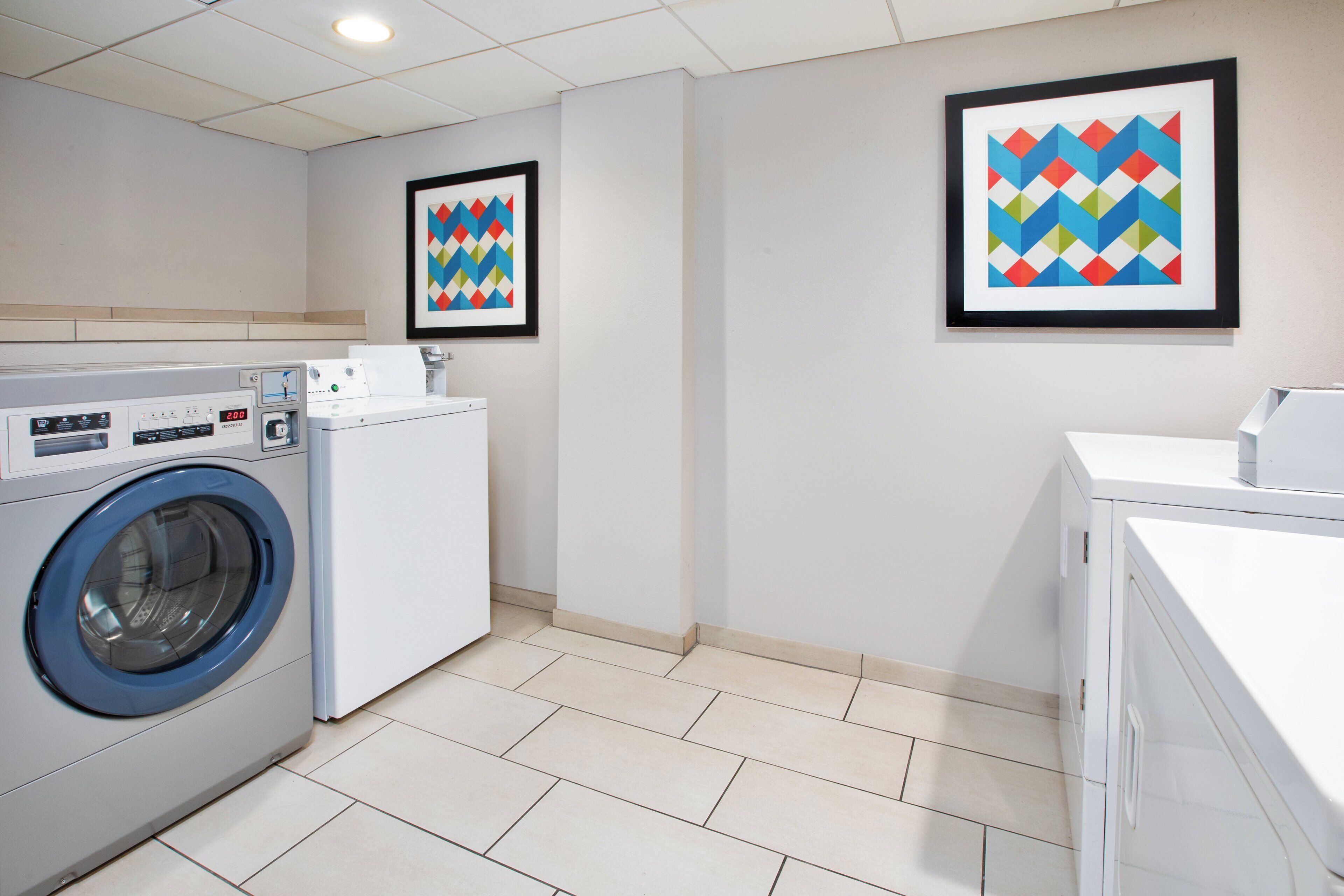 Een wasserette met een voorlader wasmachine, een droger en twee ingelijste kunstwerken aan de muur.