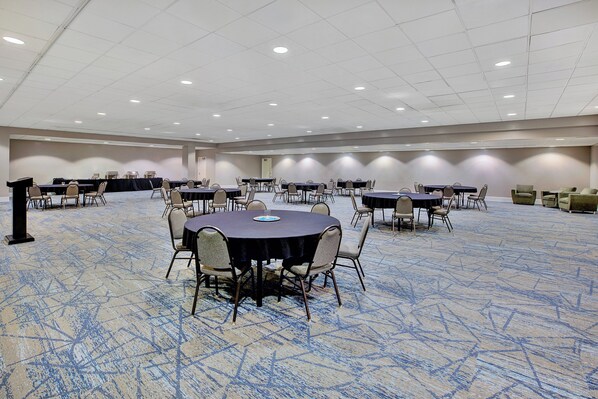 A large conference room with multiple tables and chairs, carpeted floor, and recessed lighting.