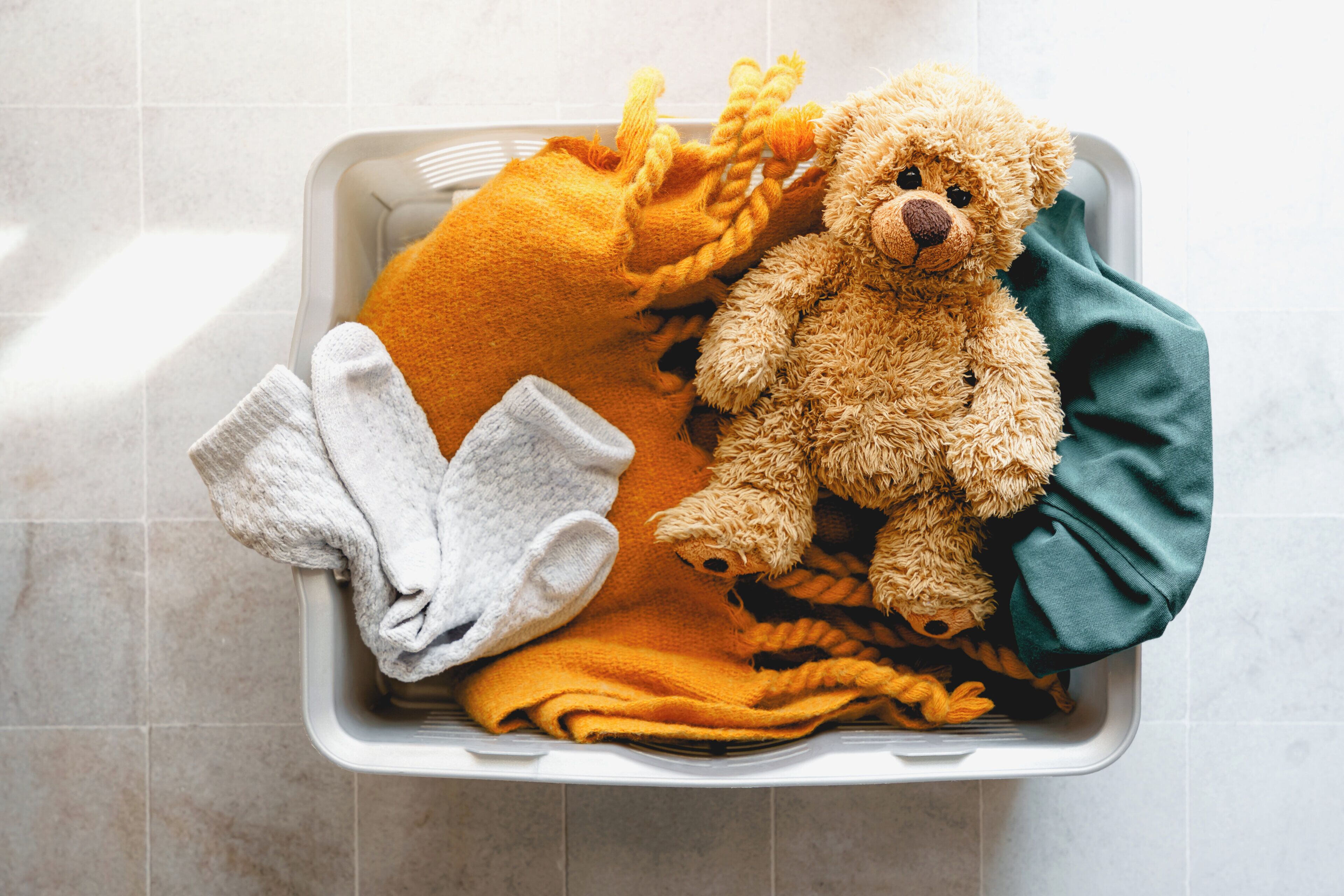 A laundry basket with a teddy bear, a yellow towel, and a white towel.