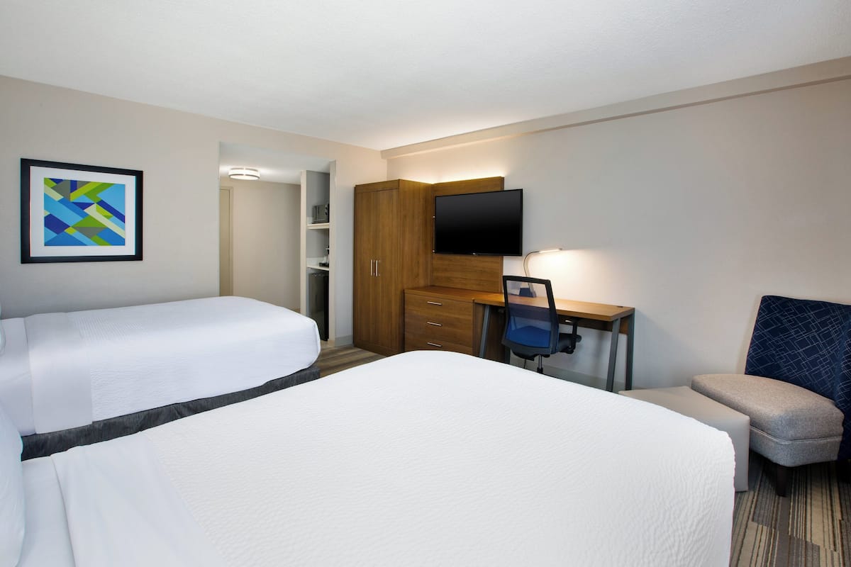 Ein Hotelzimmer mit zwei Betten, einem Schreibtisch mit Stuhl, einem Fernseher und einem gerahmten Bild an der Wand.