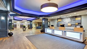 Un hall d’hôtel avec un comptoir d’accueil, un éclairage moderne et un revêtement de sol en bois.