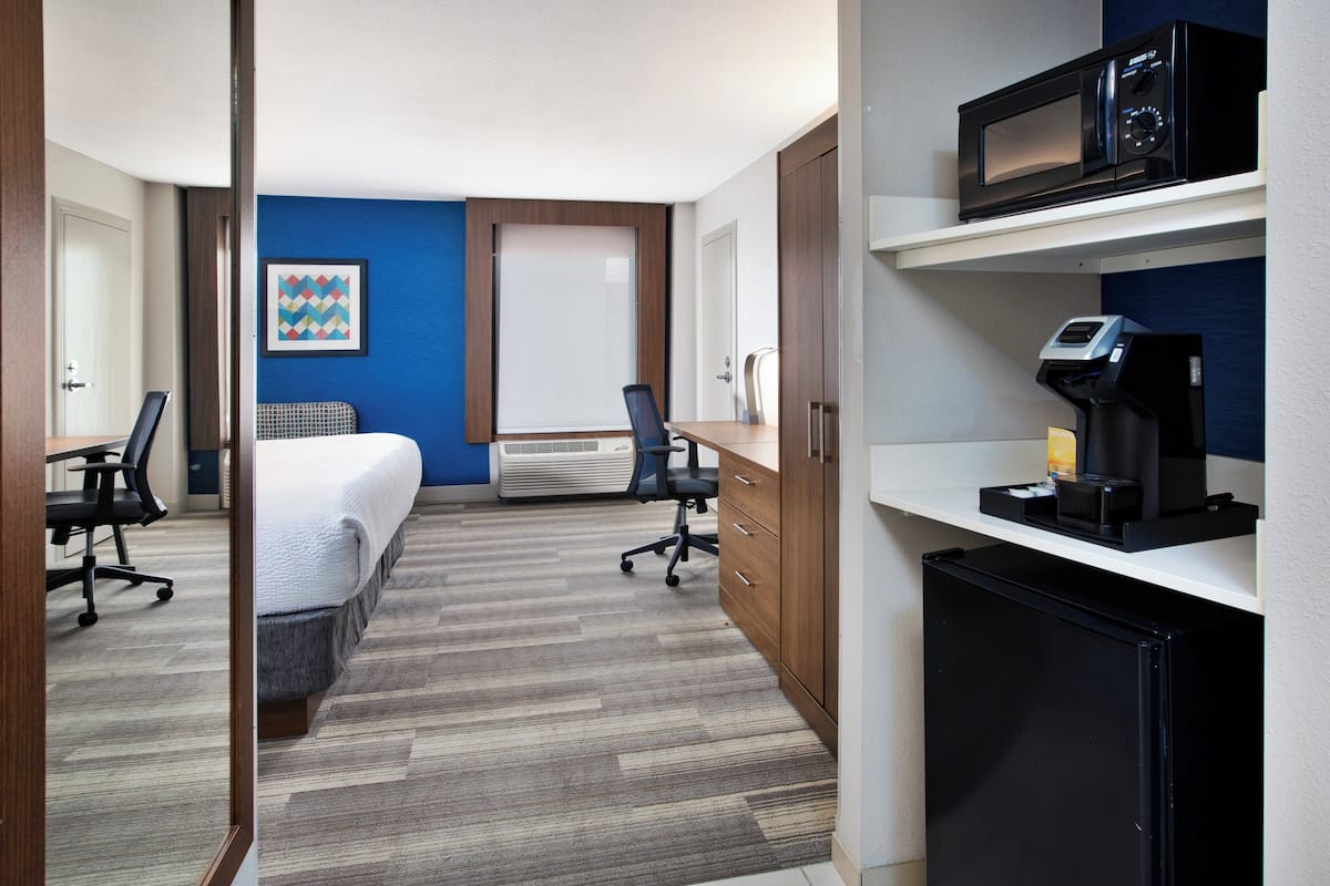 Ein Hotelzimmer mit Bett, Schreibtisch, Stühlen, einer Mikrowelle, einer Kaffeemaschine und einem kleinen Kühlschrank.