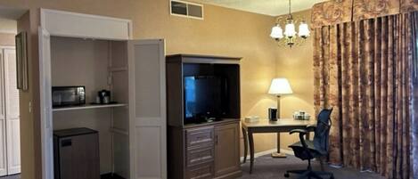 Habitación de hotel con escritorio, silla, televisión y minibar.