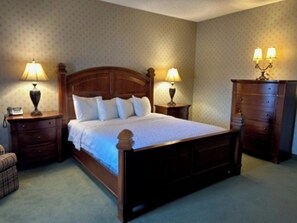 Quarto com cama de madeira, duas mesas de cabeceira com abajures, um criado-mudo e cômoda, além de parede estampada.