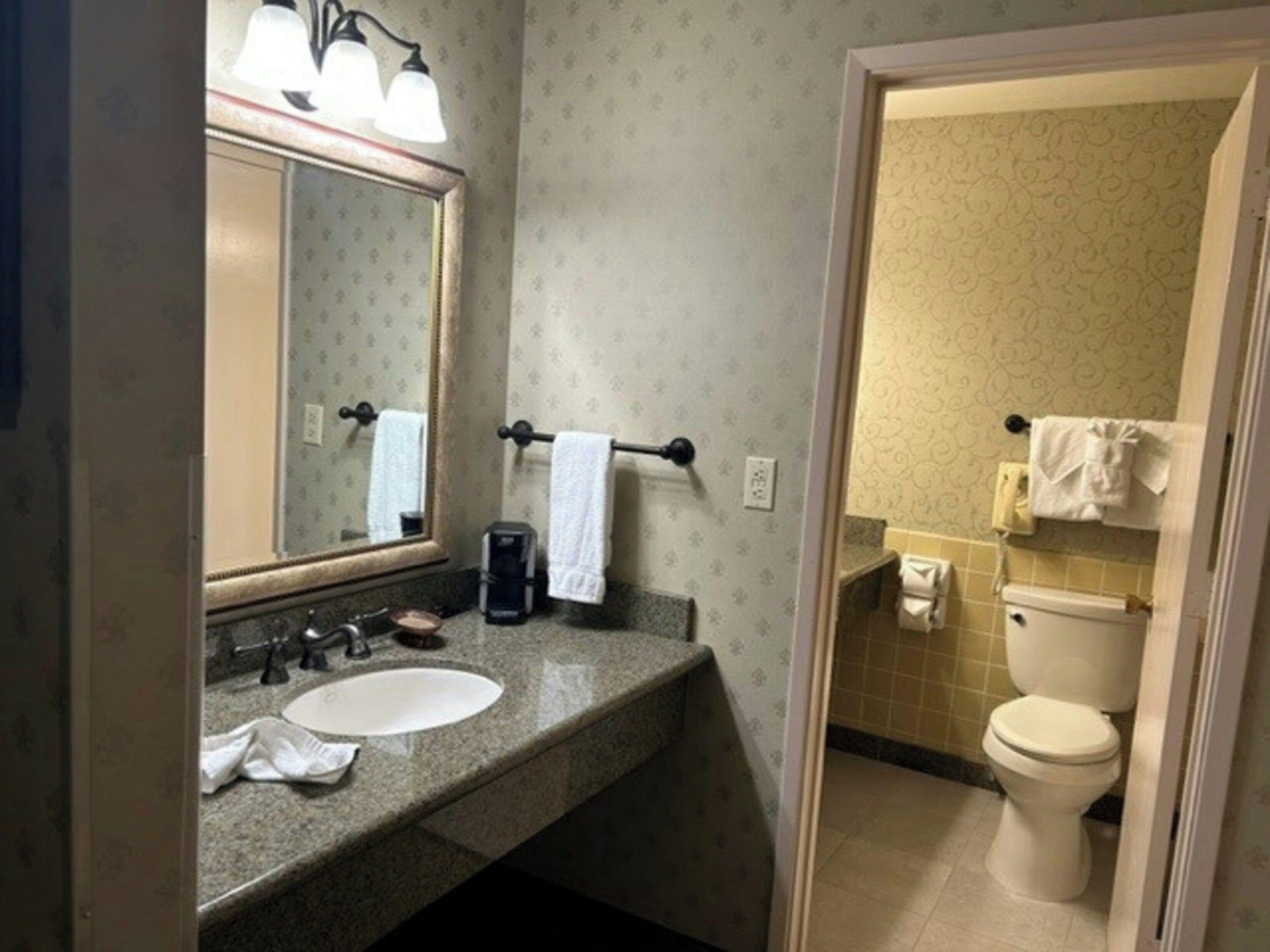 Un baño con lavamanos, espejo, toallero y inodoro.
