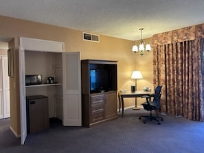 Une chambre d’hôtel équipée d’un bureau, d’une chaise, d’une télévision, d’un minibar et d’une armoire.