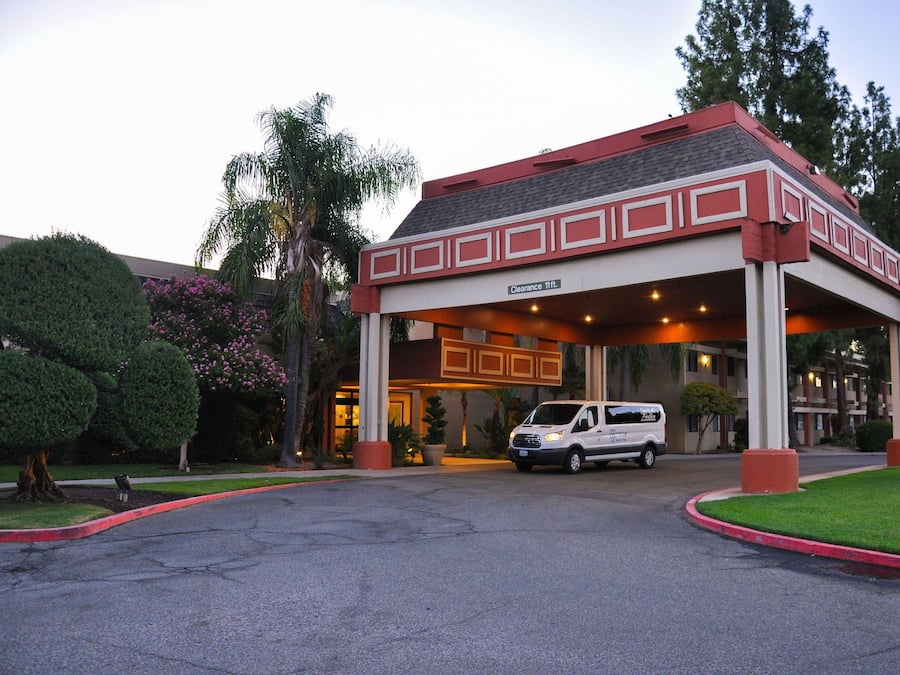 A hotel entrance with a covered waiting area, a van parked in front, and a clear sky.