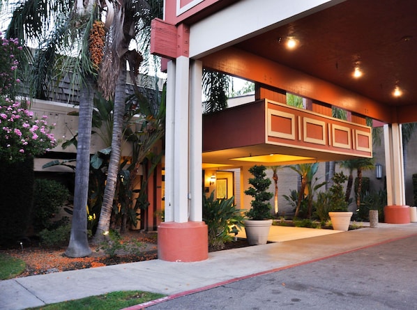 A building with a covered entrance, palm trees, and potted plants.