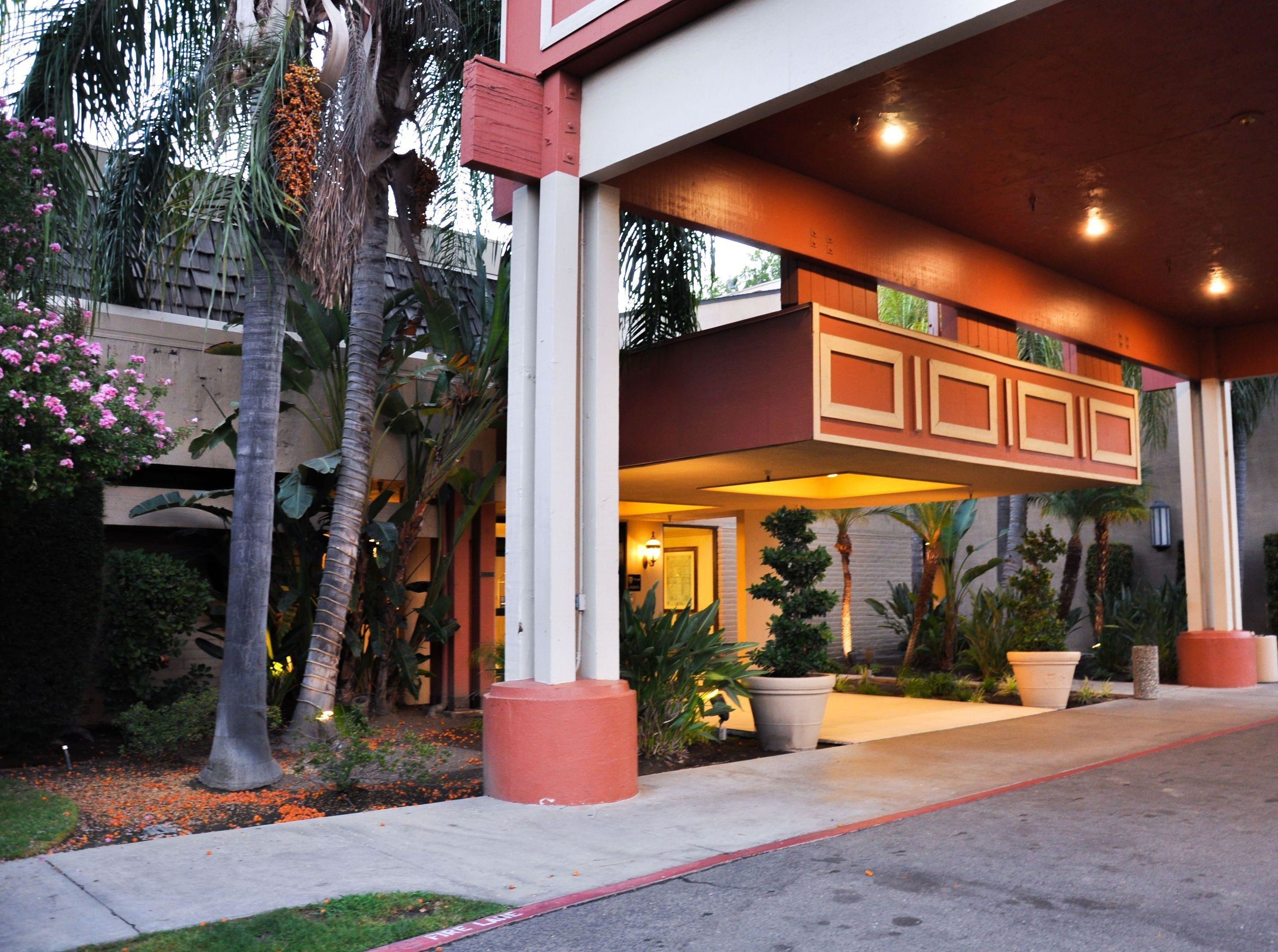 A building with a covered entrance, palm trees, and potted plants.