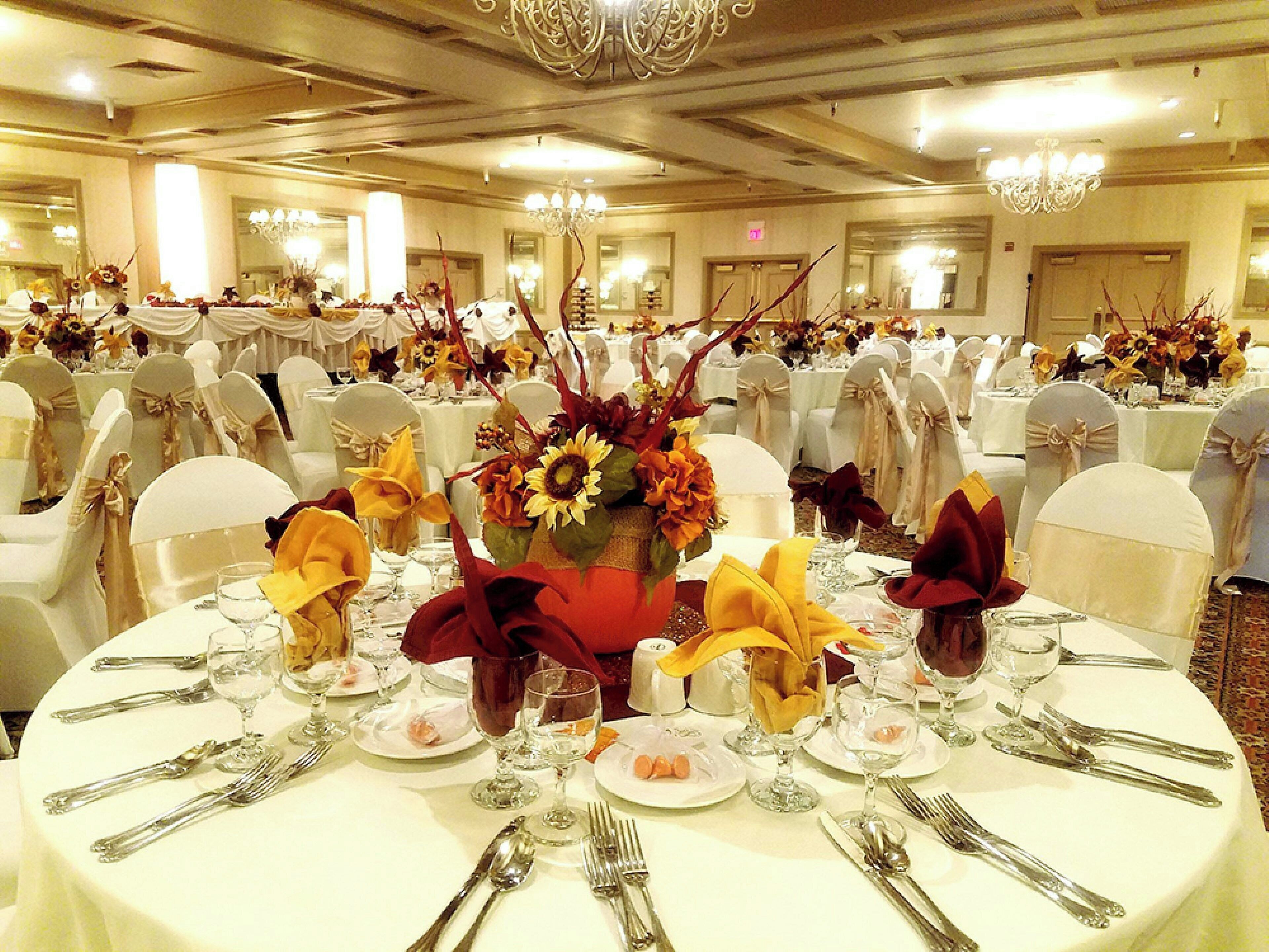 A banquet hall with round tables set for a formal event, featuring floral centerpieces and white tablecloths.